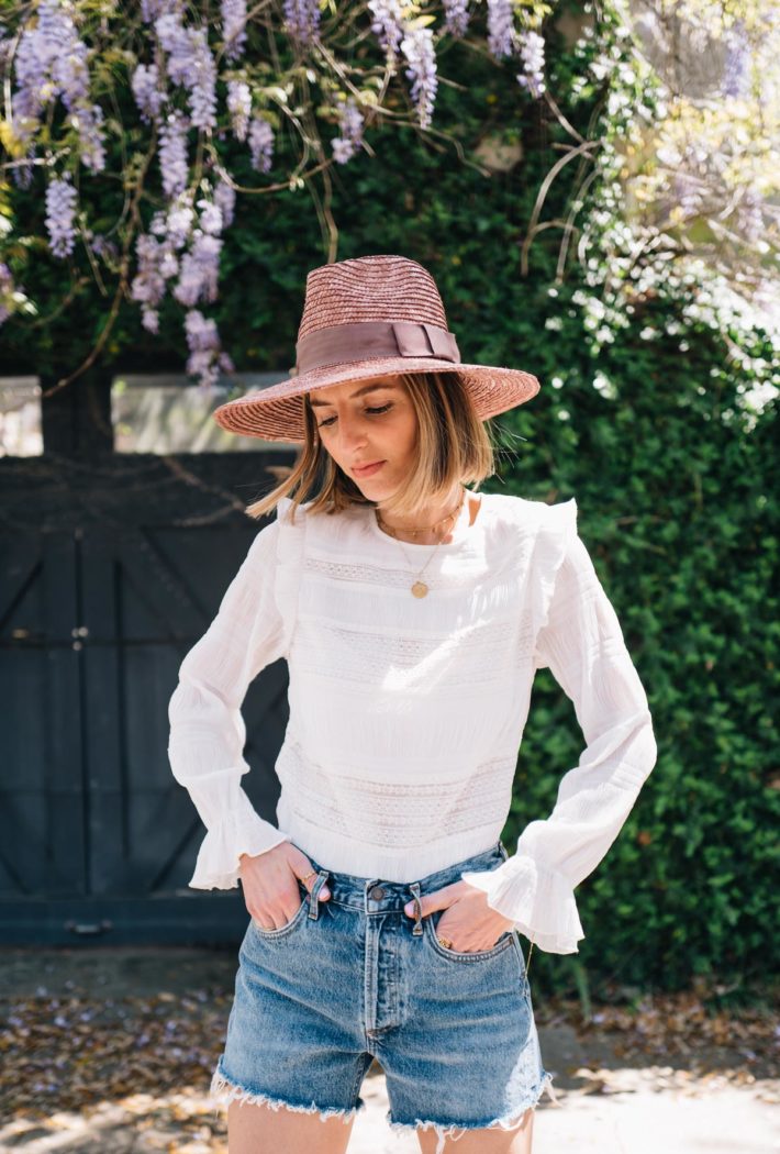 Jess Ann Kirby styles one of her favorite summer accessories, a straw hat, with classic denim shorts.