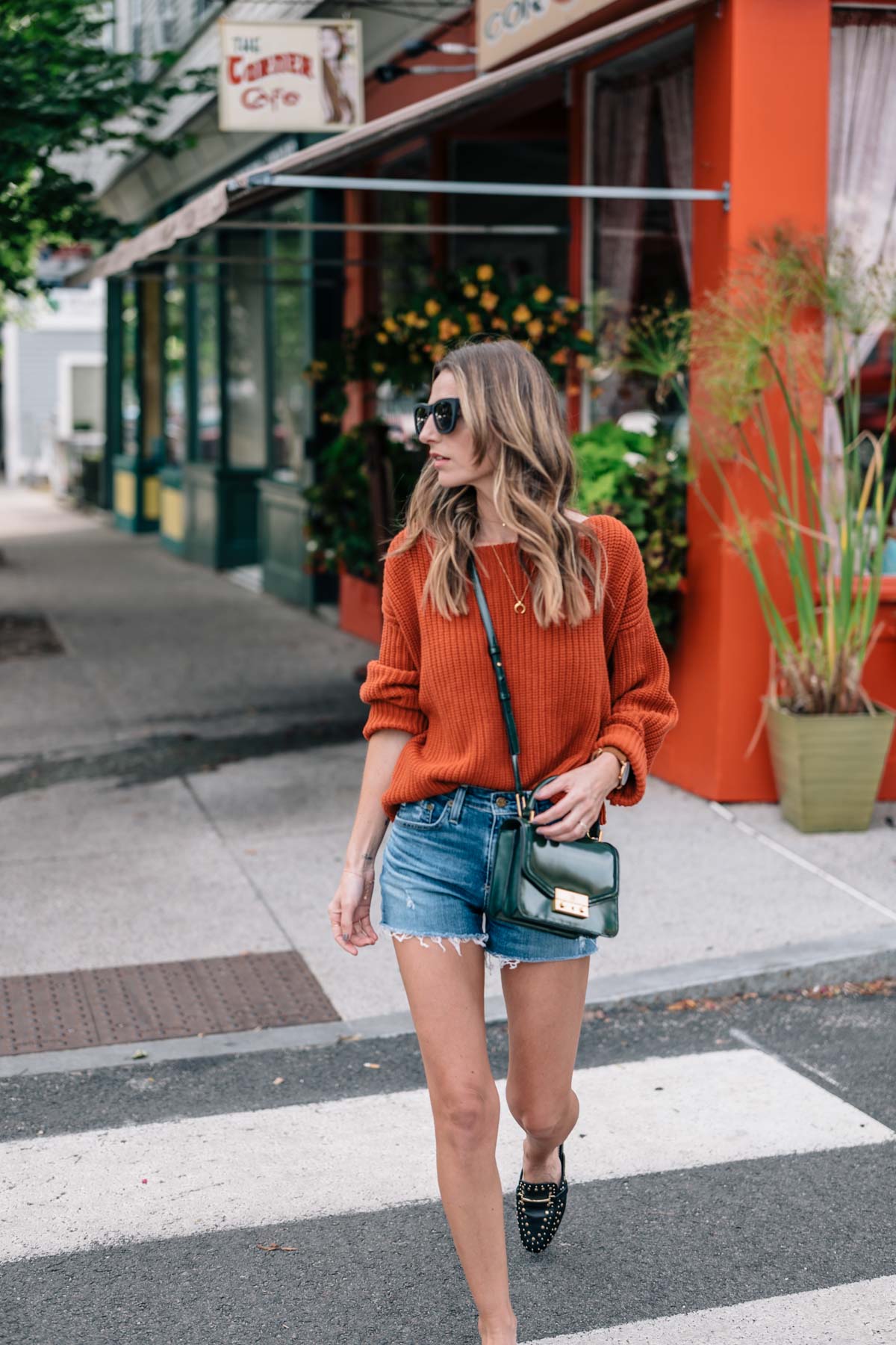 Jess Ann Kirby fall color trend street style in a chunky knit sweater, jean shorts, and slides