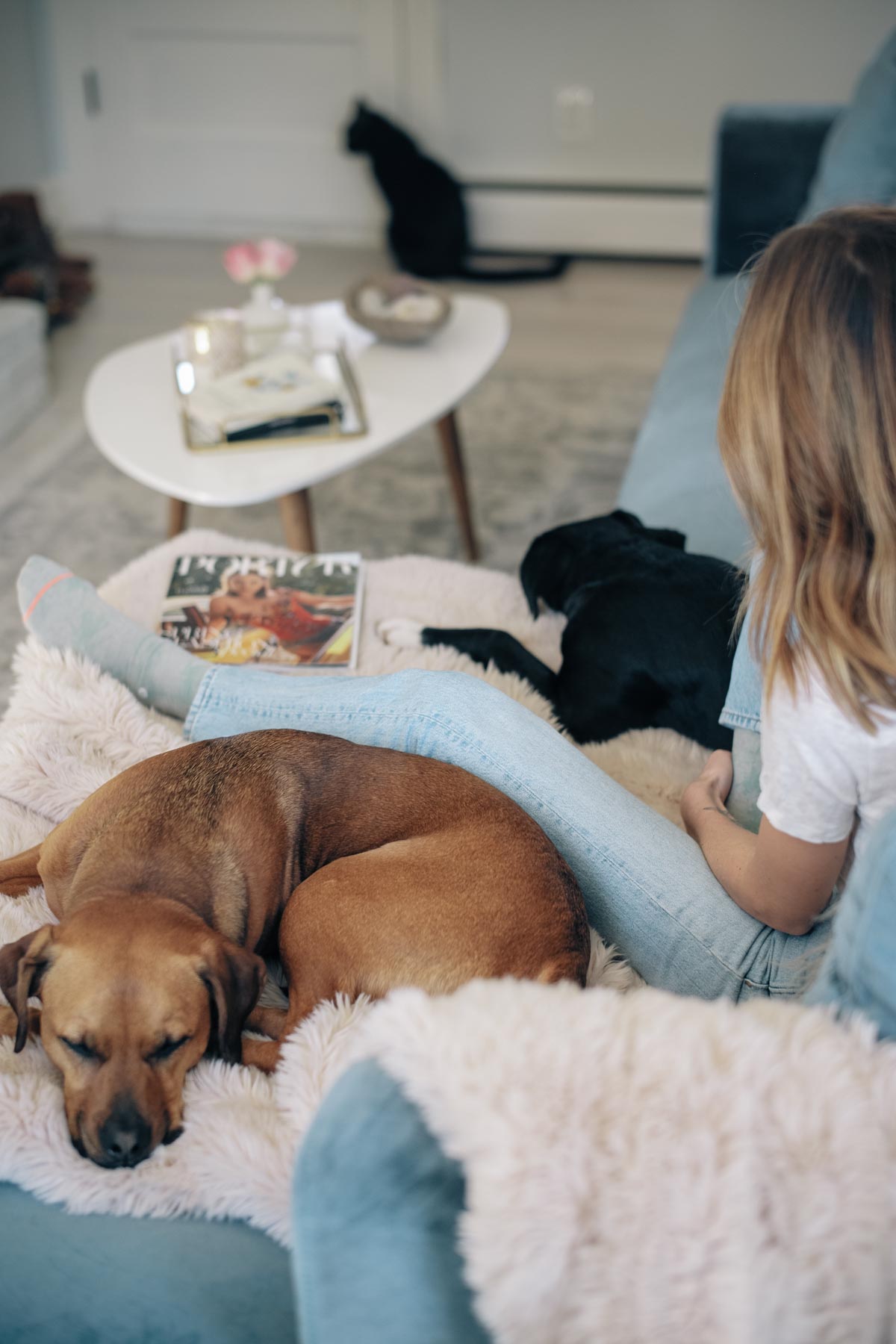 Jess Ann Kirby relaxes on her blue velvet sofa with a blush faux fur throw blanket